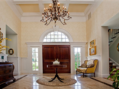 photo of Grand Foyer with great chandelier hanging from coffered ceiling, custom stained french doors with side lights and below semi-circular window