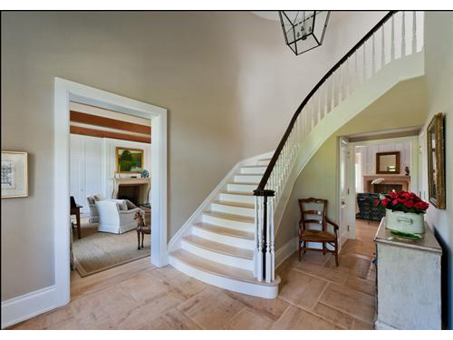 photo of foyer with doorway to left and dramatic curved staircase in center.  