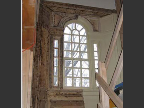 photo of ornate multi-paned arched window interior half way in process of lead paint removal