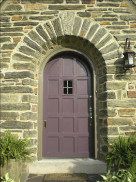 photo of plum painted door with lavender trim, with 4 pane window.  Stone step in front and set into a stone roman arhc