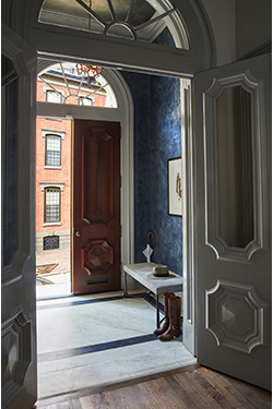 photo of entrance foyer showing inner white door, exterior stained door, blue venetian plaster on foyer wall and sunburst windows above doors